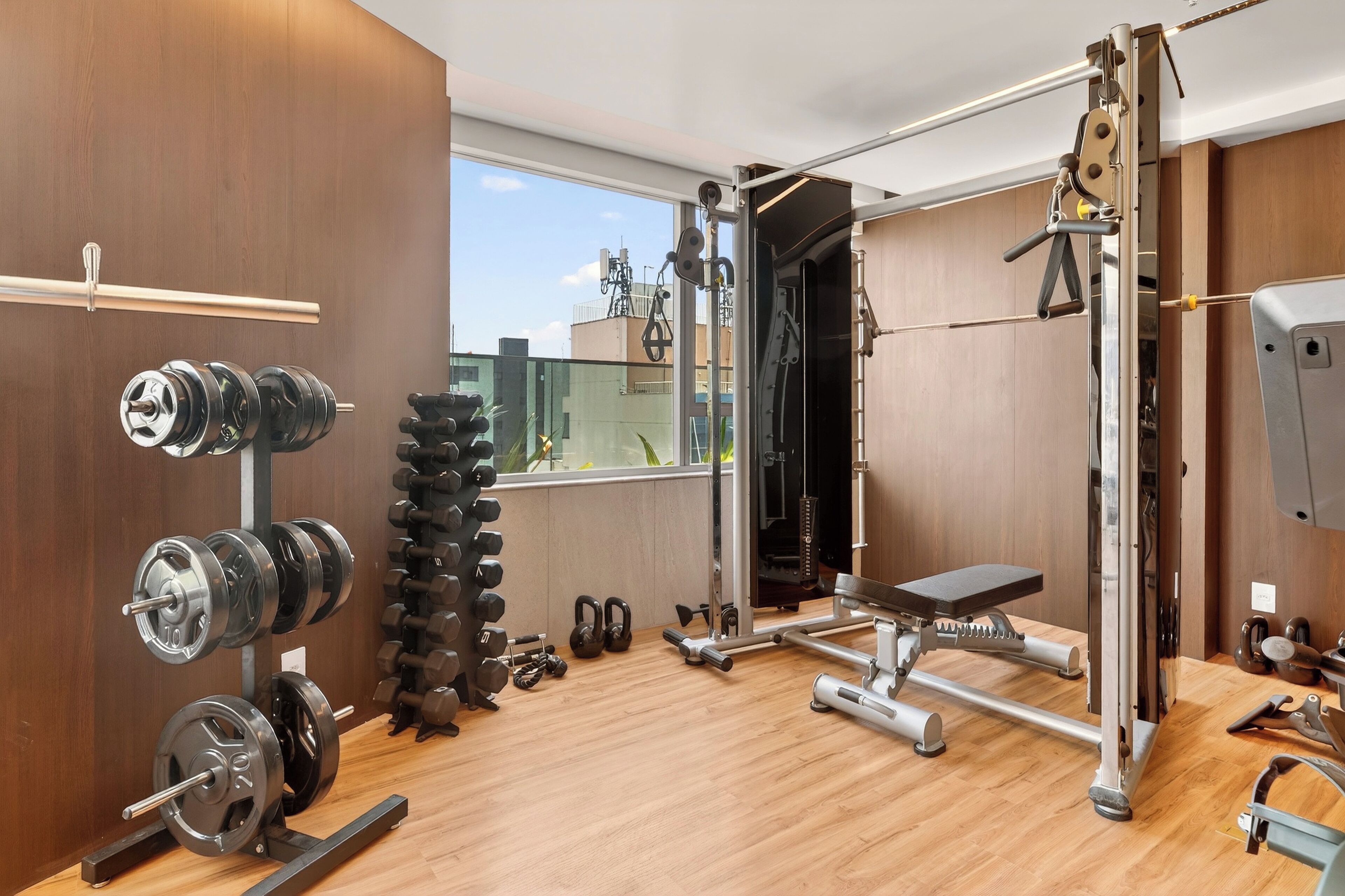 Ein modernes Fitnessstudio mit Krafttrainingsgeräten, einer Bank und Blick auf die Stadt durch große Fenster.
