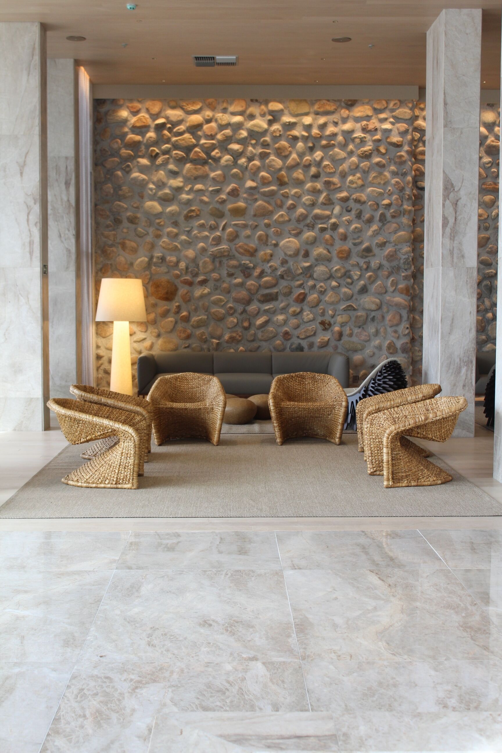 Un hall con pared de piedra, un sofá y sillones de mimbre.