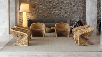 Un hall con pared de piedra, un sofá y sillones de mimbre.