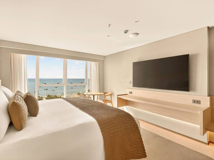 Hotelkamer met een groot bed, een aan de muur bevestigde televisie, een bureau en uitzicht op de oceaan.