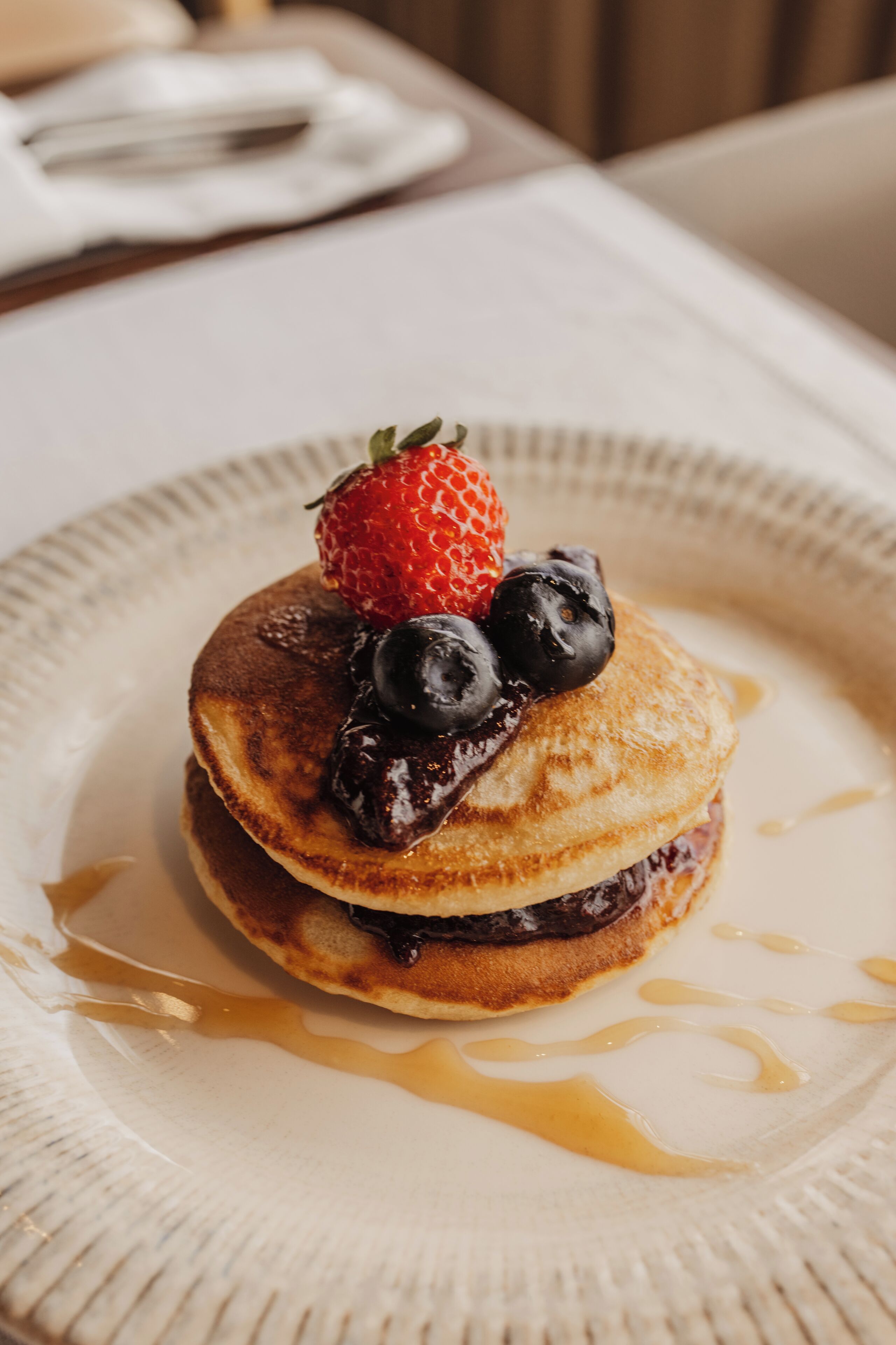 A plate with pancakes topped with berries and syrup.