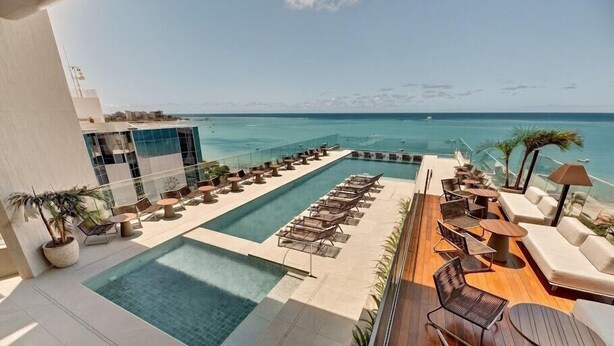 Un espace piscine aménagé sur le toit, avec des chaises longues et une vue sur l’océan.