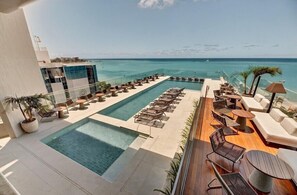 Un área de piscina en la azotea con sillones de descanso y vista al océano.