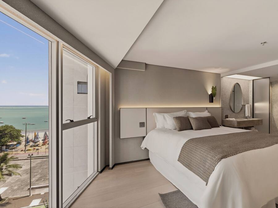 Un dormitorio moderno con una cama grande, una mesita de noche, un espejo y vistas a la playa.