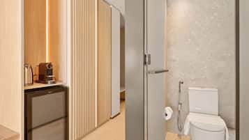 A compact kitchenette with a coffee maker and a mini-fridge, a sliding wooden partition, and a modern bathroom with a marble wall and a toilet.