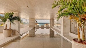 Un couloir donnant sur une piscine, agrémenté de plantes en pot et offrant une vue sur l’océan.