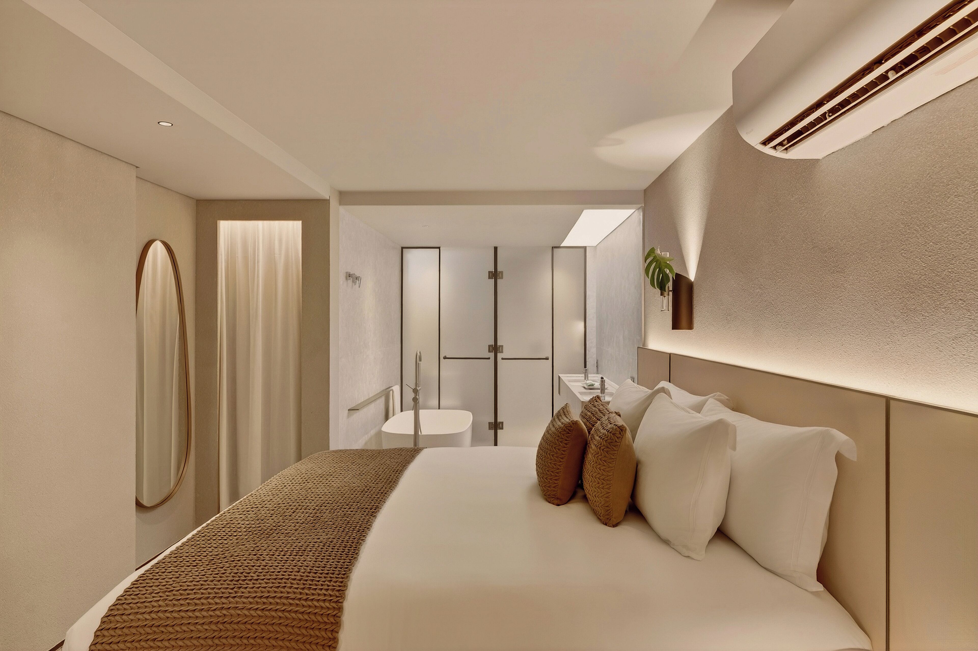 Una habitación de hotel moderna con una cama grande, una mesita de noche pequeña, un espejo y una zona de ducha.