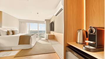 Habitación de hotel moderna con cama, escritorio con cafetera, televisor y vista al mar.