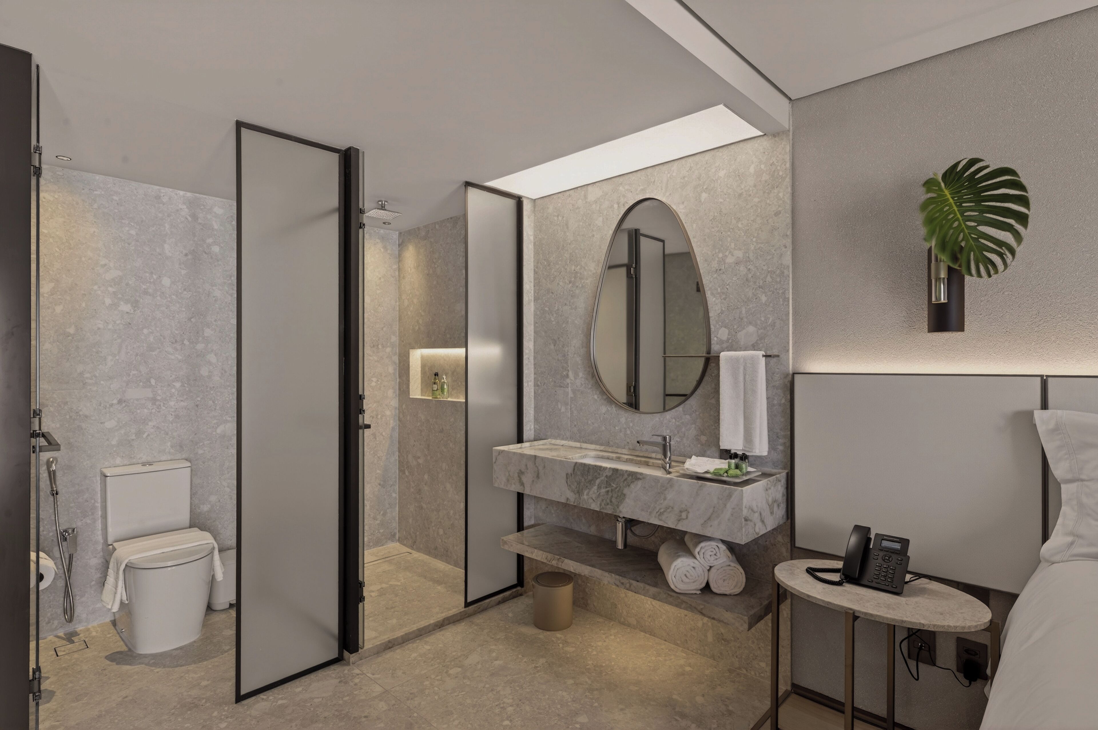 A modern bathroom with a marble sink, a large mirror, a toilet, and a small table with a phone.