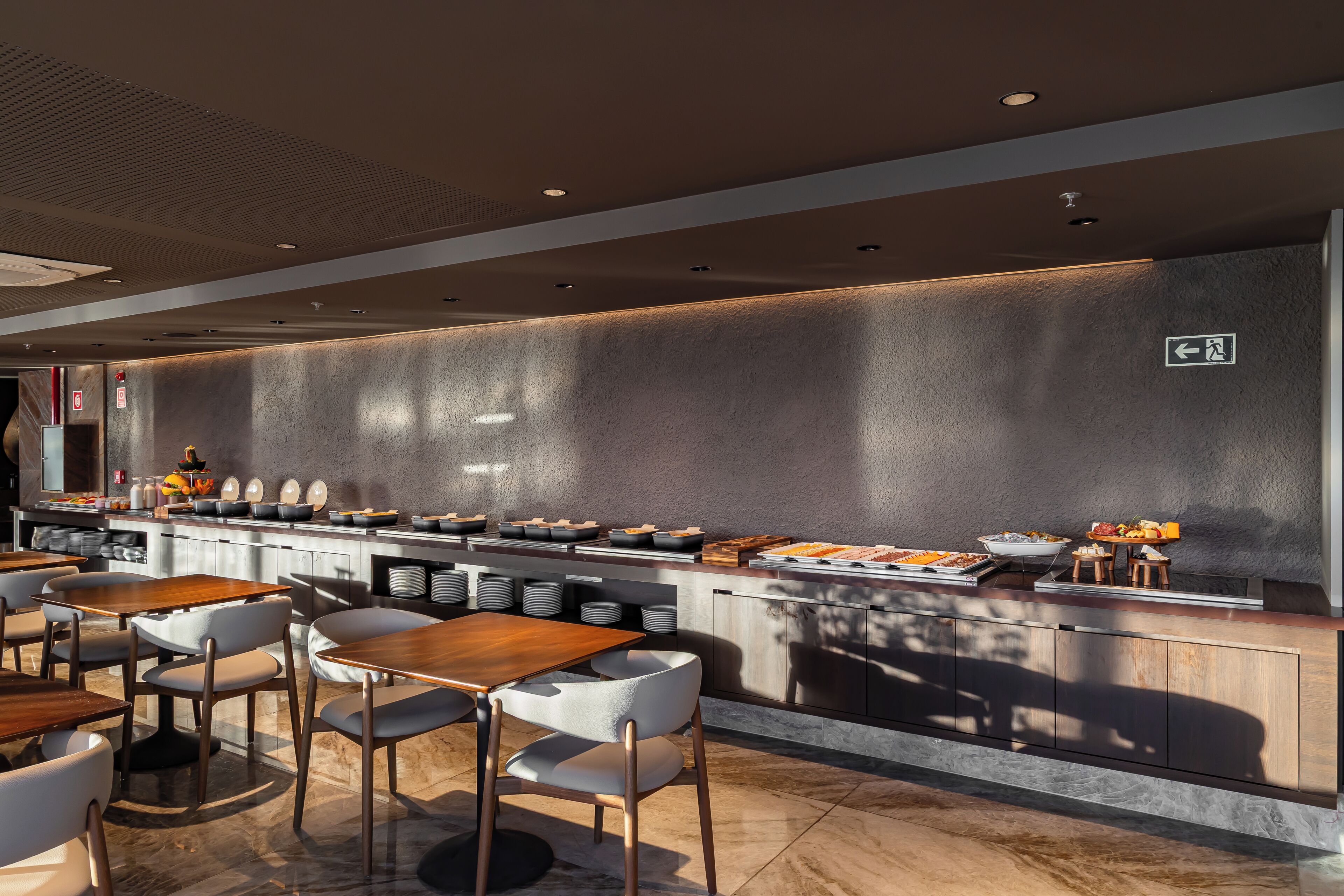Un restaurant modern amb una barra llarga, diverses zones de seients i un panell de menú penjat a la pared.