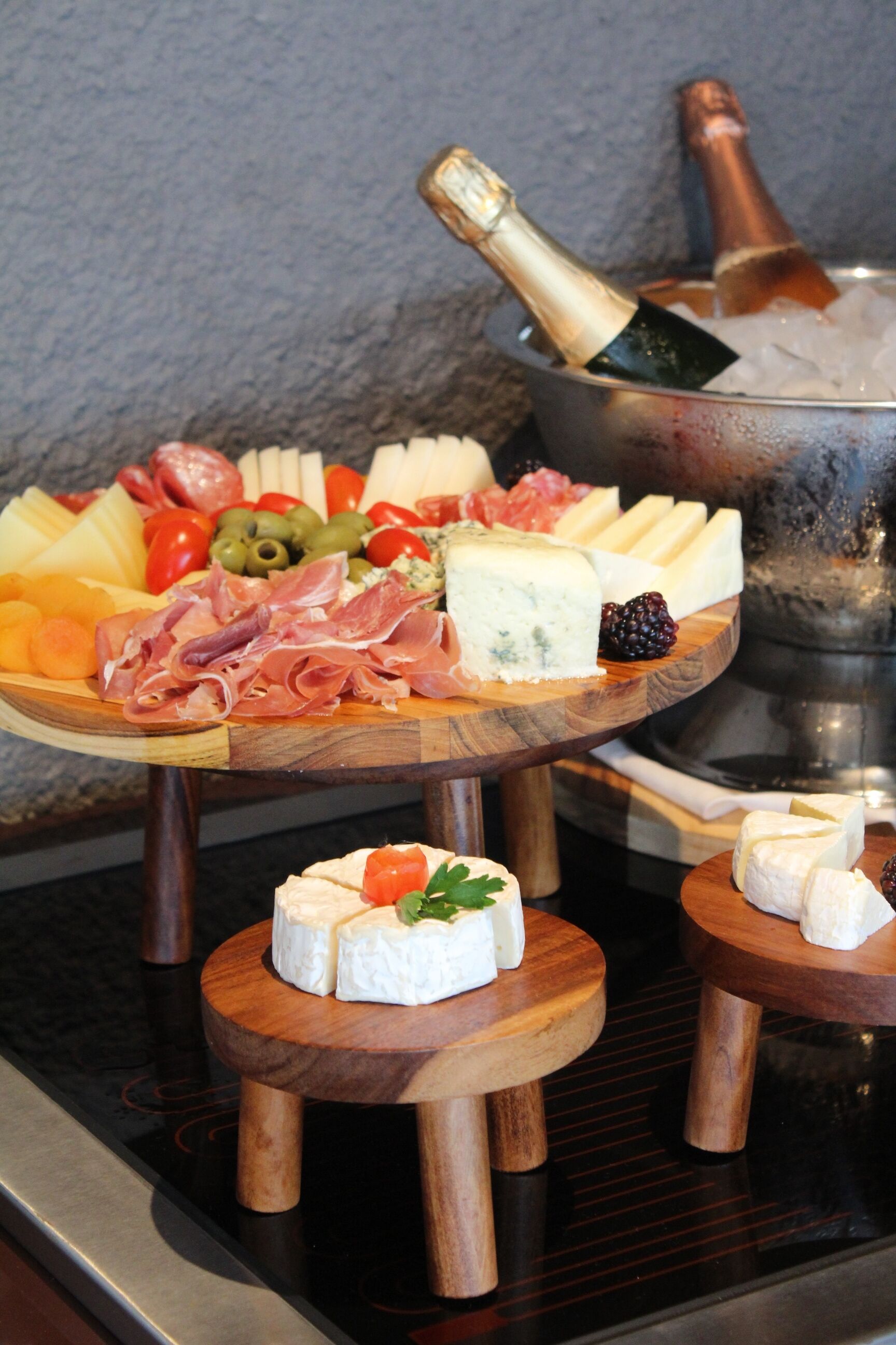 Une planche de charcuterie garnie de différents fromages, de viandes et de fruits, accompagnée d’une bouteille de champagne dans un verre.