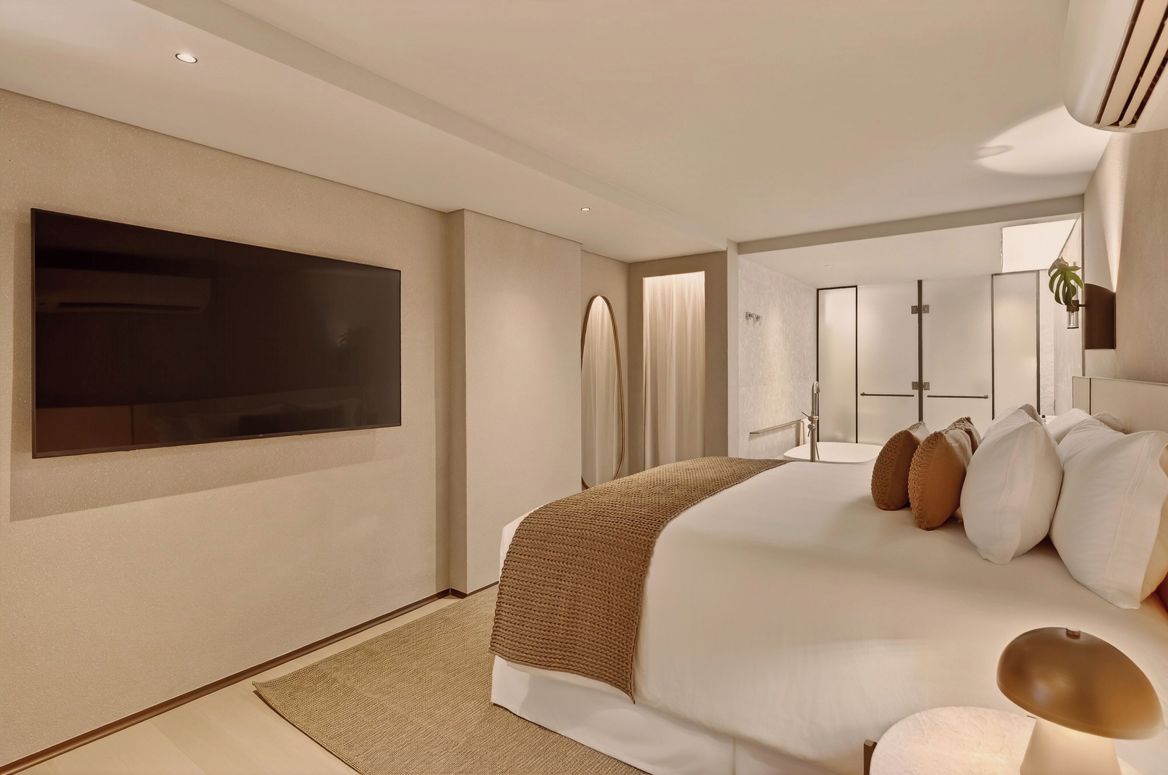 Una habitación de hotel moderna con una cama grande, un televisor de pantalla plana, un baño con espejo y una planta.