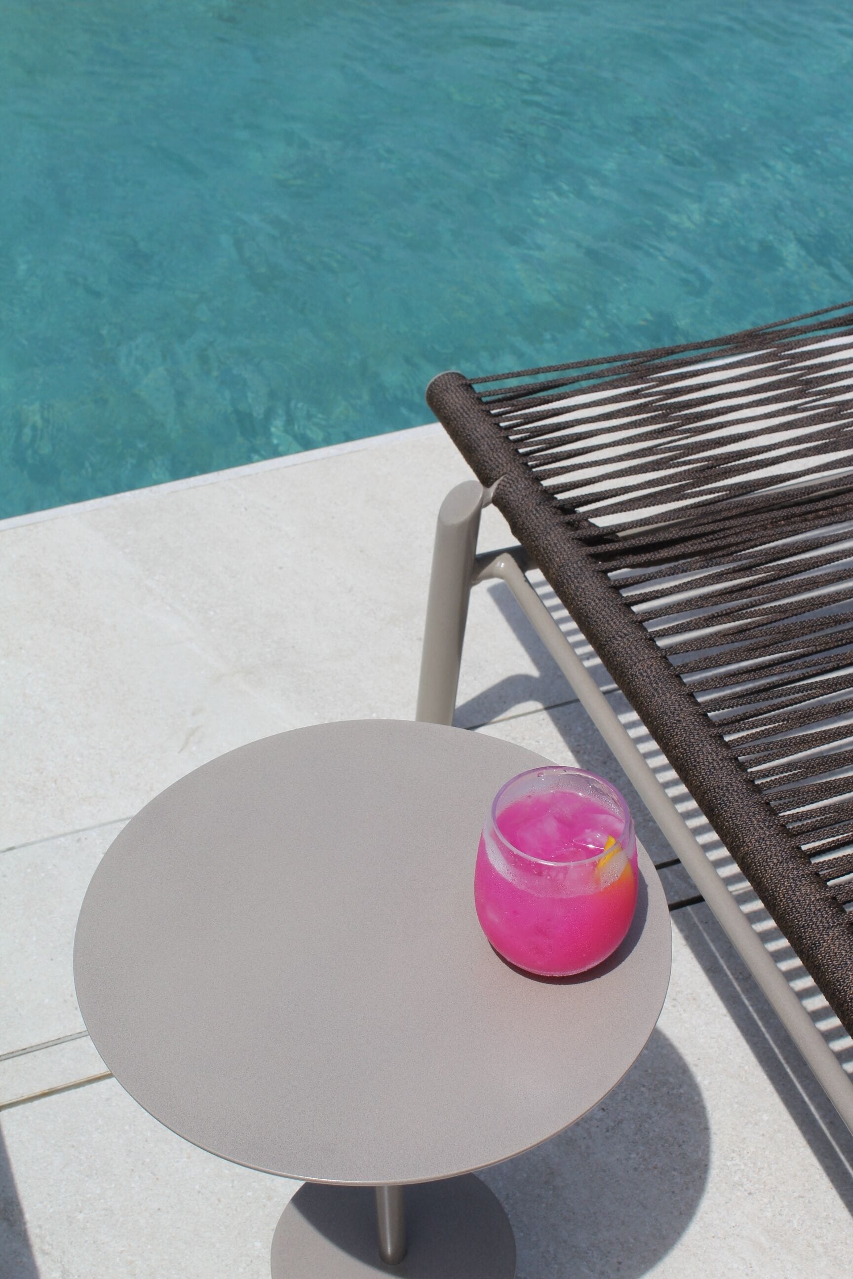 Une table ronde avec une boisson rose, une chaise et une piscine en arrière-plan.