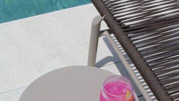 Une table ronde avec une boisson rose, une chaise et une piscine en arrière-plan.