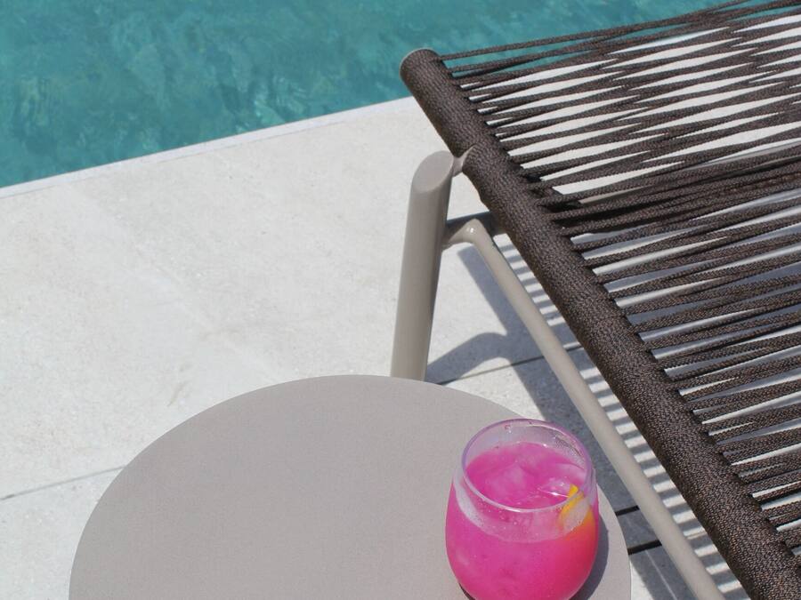 Une table ronde avec une boisson rose, une chaise et une piscine en arrière-plan.