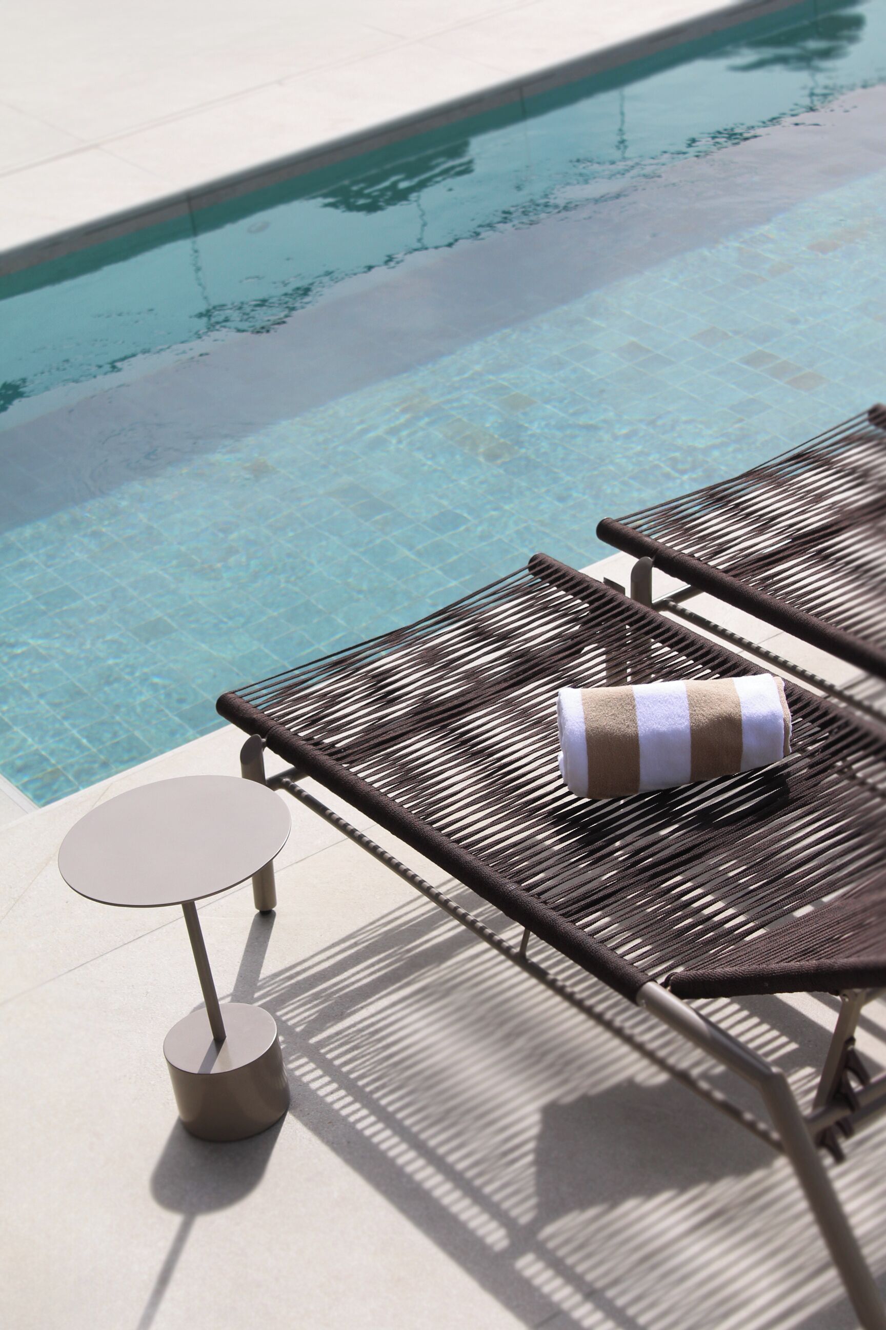 Un espace aménagé au bord de la piscine, avec deux chaises longues et une petite table, dont une est agrémentée d’une serviette à rayures.