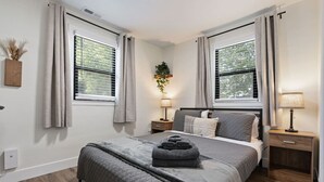 Een slaapkamer met een bed, twee nachtkastjes, een lamp, gordijnen voor het raam en een wandplant.
