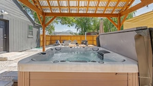 Een hottub onder een houten pergola, met uitzicht op een huis en bomen.