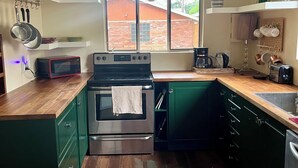 Cozinha com micro-ondas, fogão e forno. Há uma janela com vista para uma casa.
