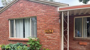Uma casa de tijolos com o número '1252' na parede, uma janela e um alpendre com um vaso de planta.