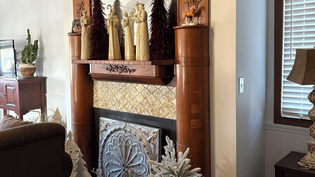 Une cheminée ornée de chevaux et de figurines décoratives, un sapin de Noël et un miroir au motif géométrique.