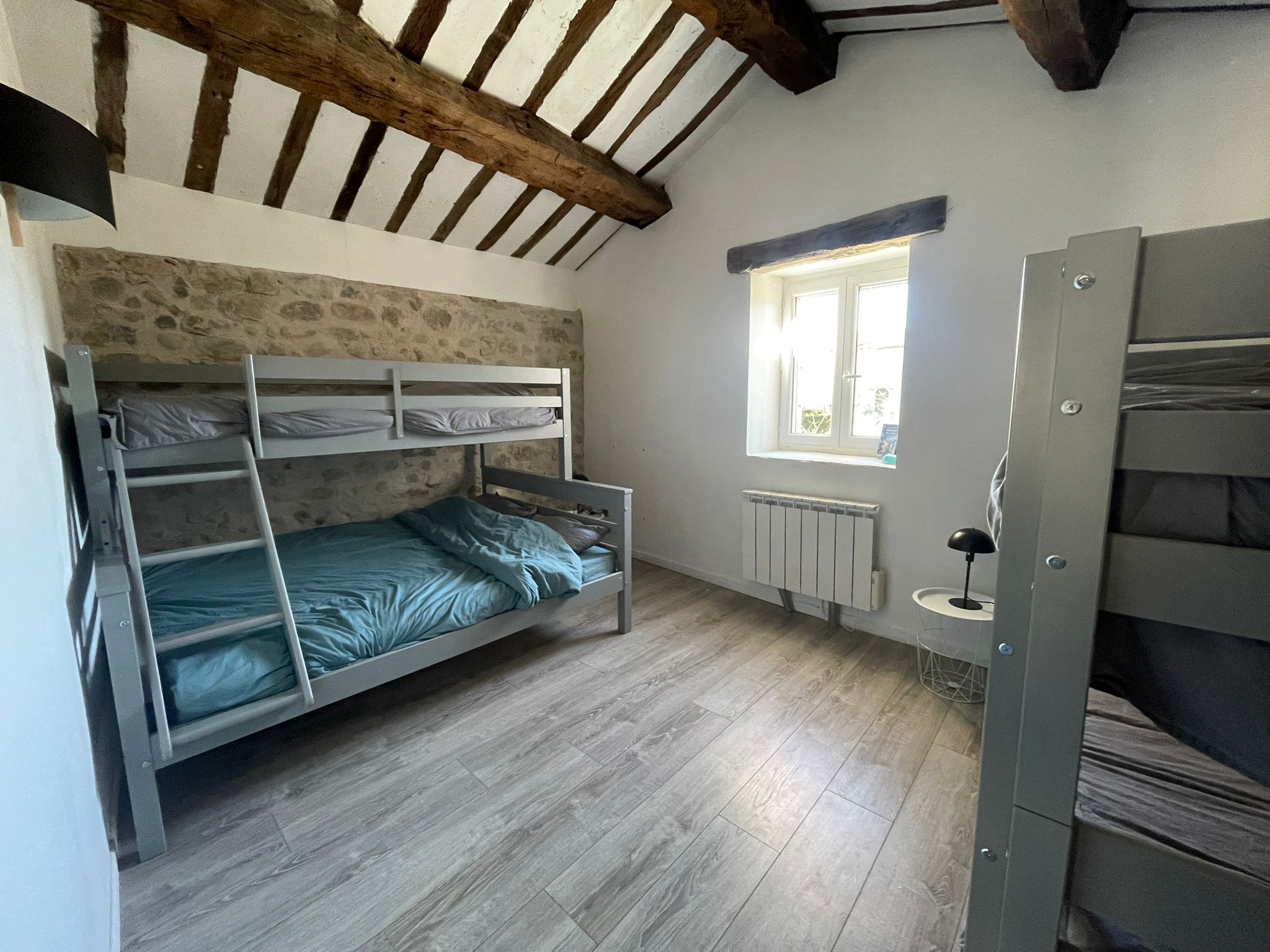 A dormitory room with bunk beds, a window, a radiator, and a wooden ceiling.