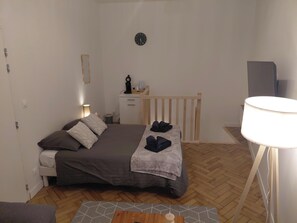 Un dormitorio pequeño y ordenado con cama, mesita de noche, lámpara y un reloj en la pared.