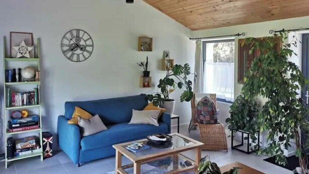 A living room with a blue sofa, a wooden ceiling, a clock, and a bookshelf. - Charming little house in the countryside (La Garnache)