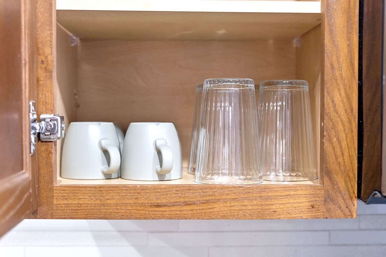 A wooden cabinet with two white mugs and two clear glasses.