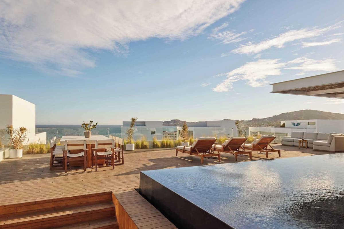 Une terrasse sur le toit avec une piscine, des chaises longues et un espace repas offrant une vue sur la mer.