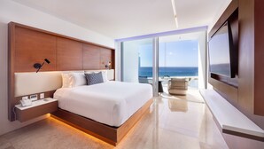 Une chambre d’hôtel moderne dotée d’un grand lit, de commandes situées à proximité du lit, d’une télévision à écran plat et d’un balcon offrant une vue sur l’océan.