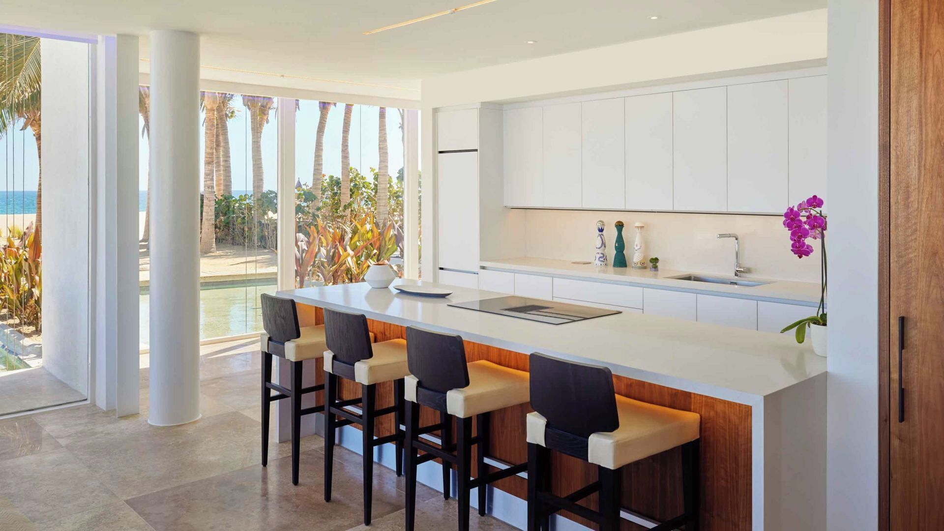 A modern kitchen with a large island, bar stools, and a view of a pool and palm trees.