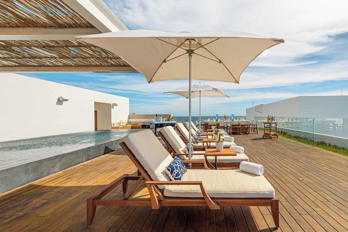 Un salon sur le toit, doté d’une terrasse en bois, de chaises longues et de parasols, offrant une vue sur une marina.