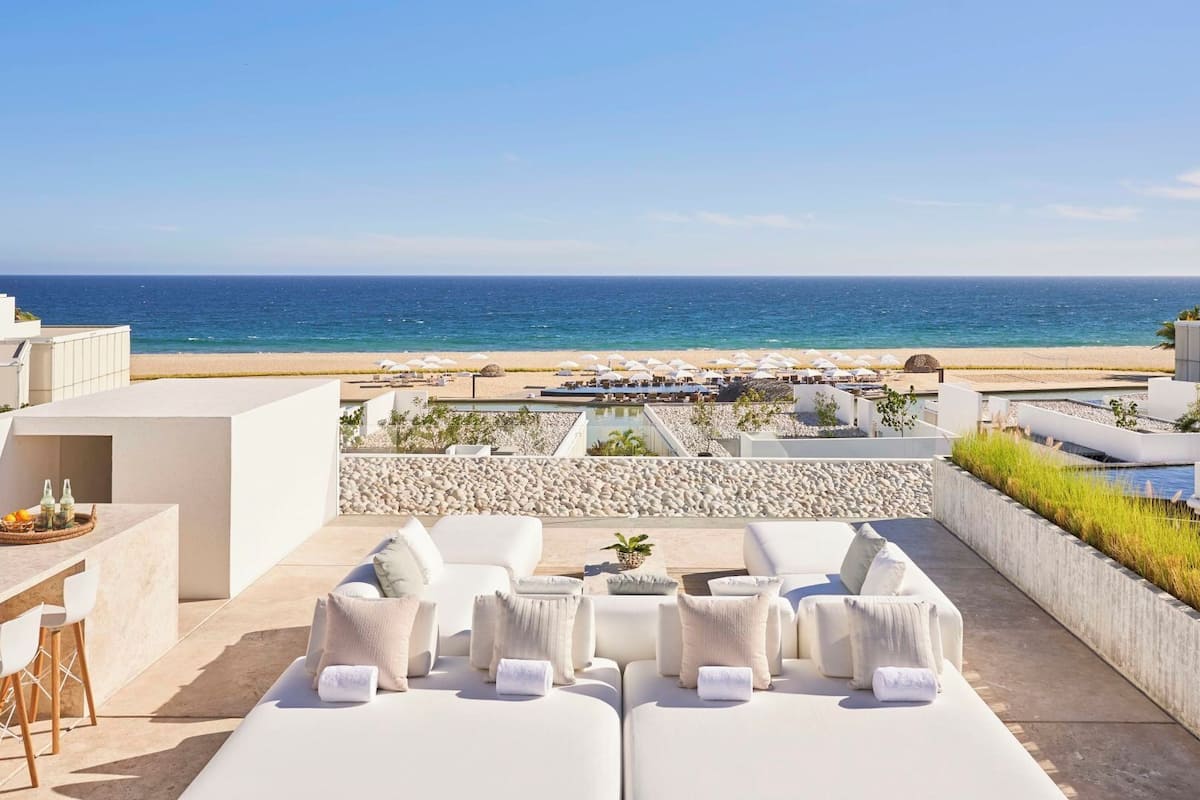 Une terrasse sur le toit, avec des chaises longues blanches et une vue sur la plage et l’océan.
