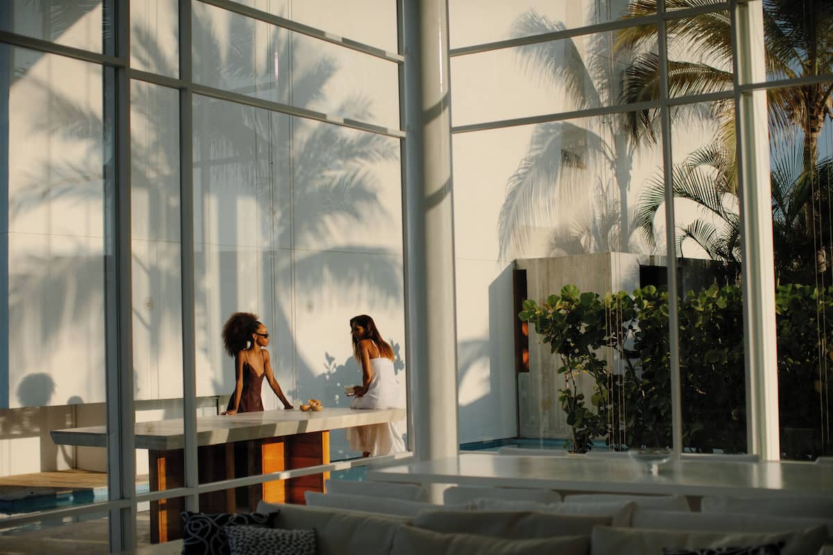 Un vaste espace intérieur doté de grandes fenêtres, d’une piscine et d’un coin salon offrant une vue sur les palmiers.