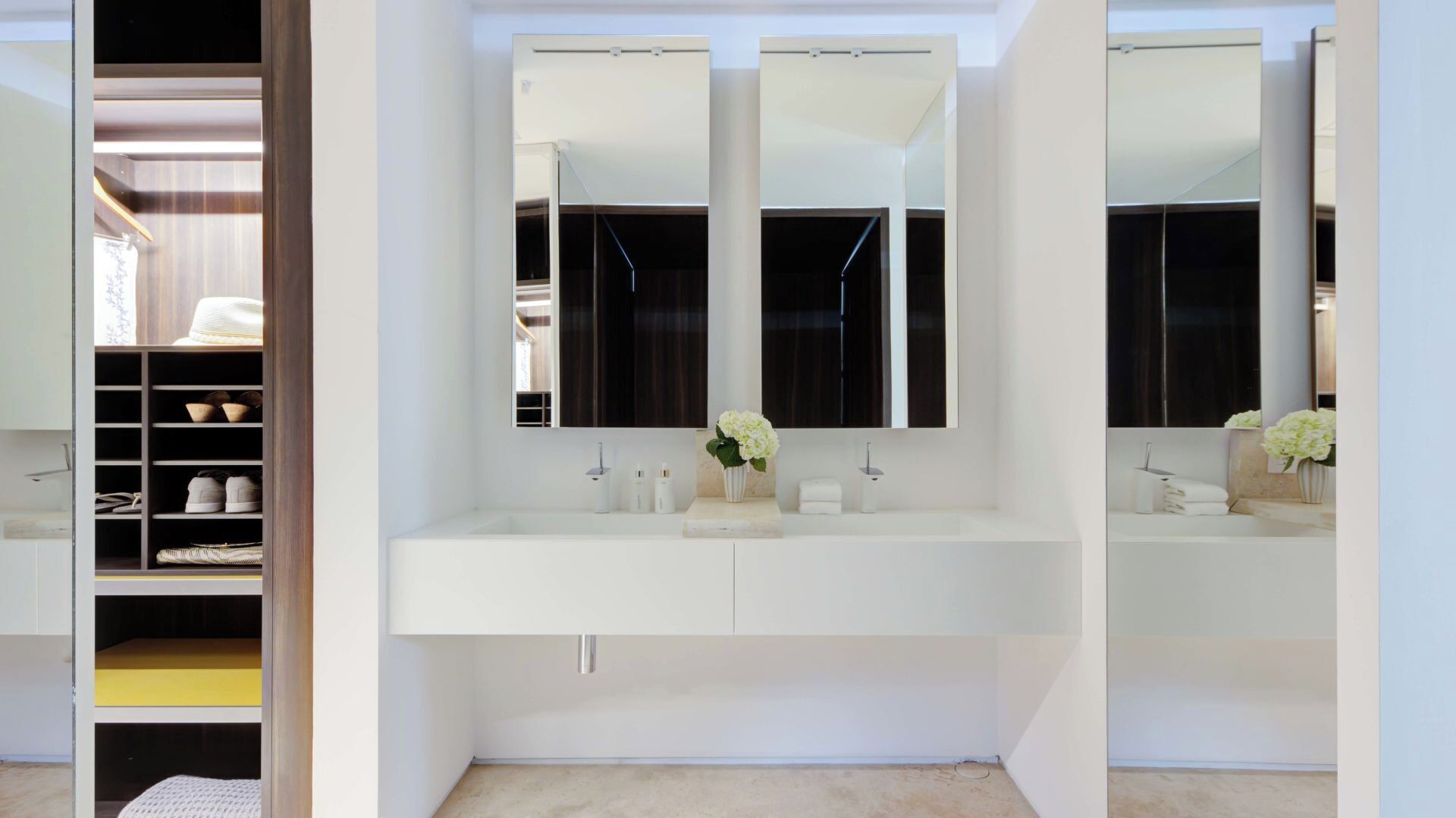 A modern bathroom with a large mirror, two sinks, and a walk-in closet with shelves.