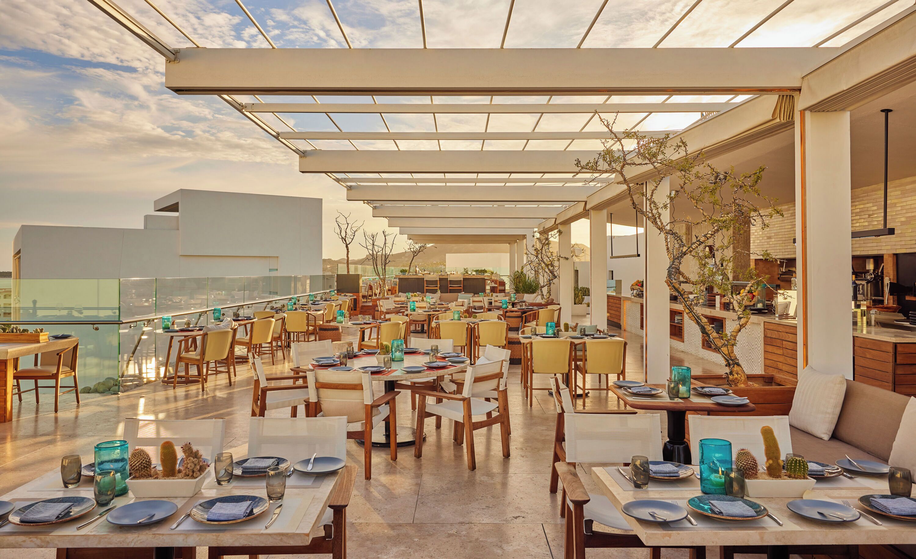 An outdoor dining area with tables and chairs, a glass railing, and a view of the cityscape.