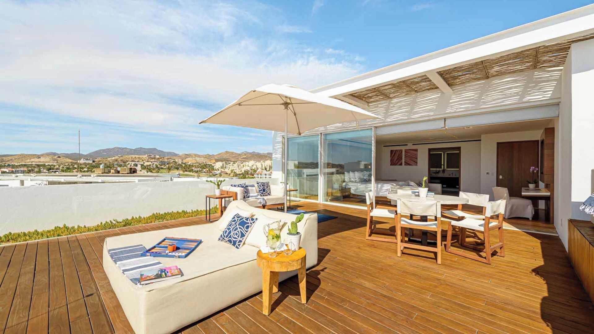 Un espacio al aire libre moderno con terraza de madera, un sofá y una mesa de comedor con sillas.