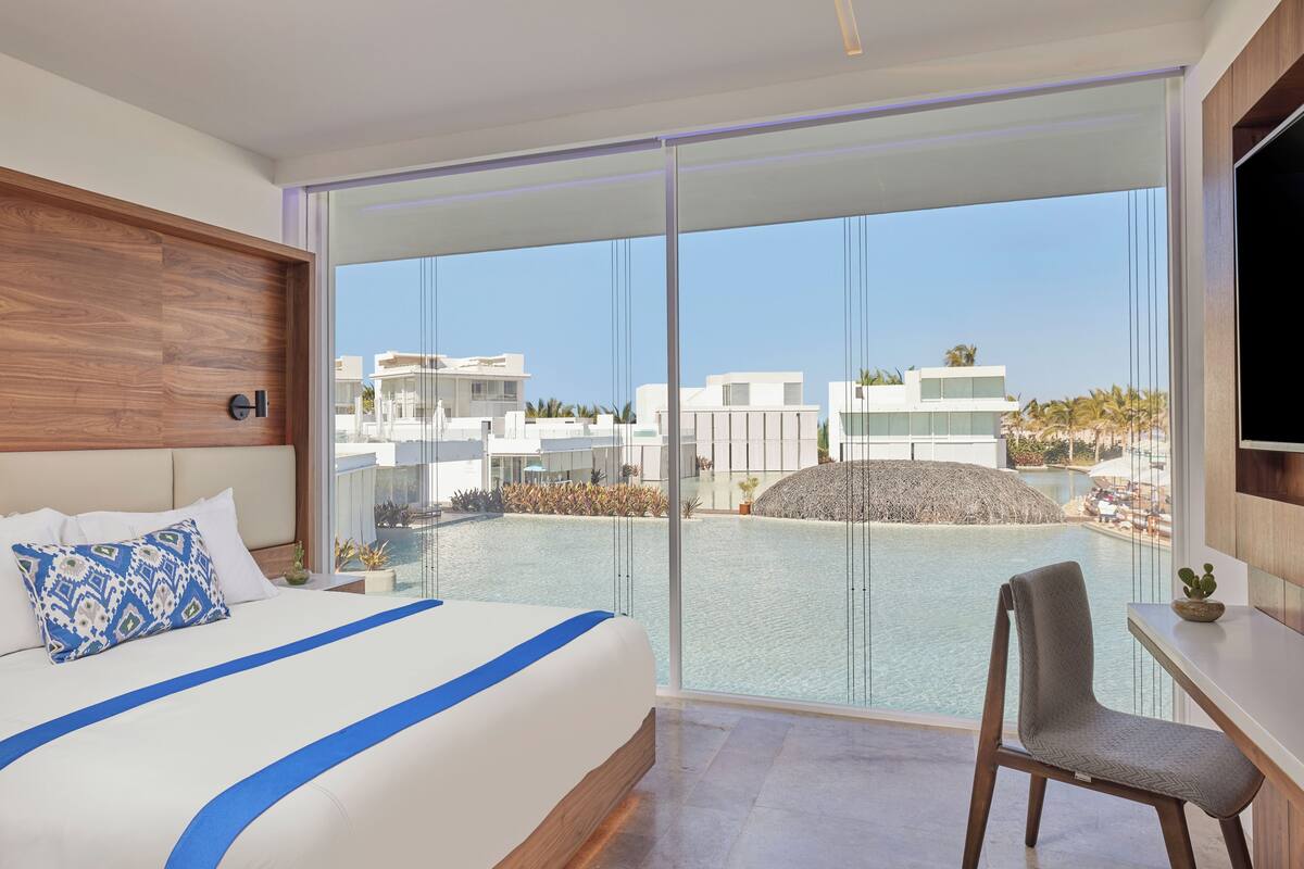 Une chambre d’hôtel moderne avec un grand lit, un bureau et une vue sur une piscine et des immeubles.