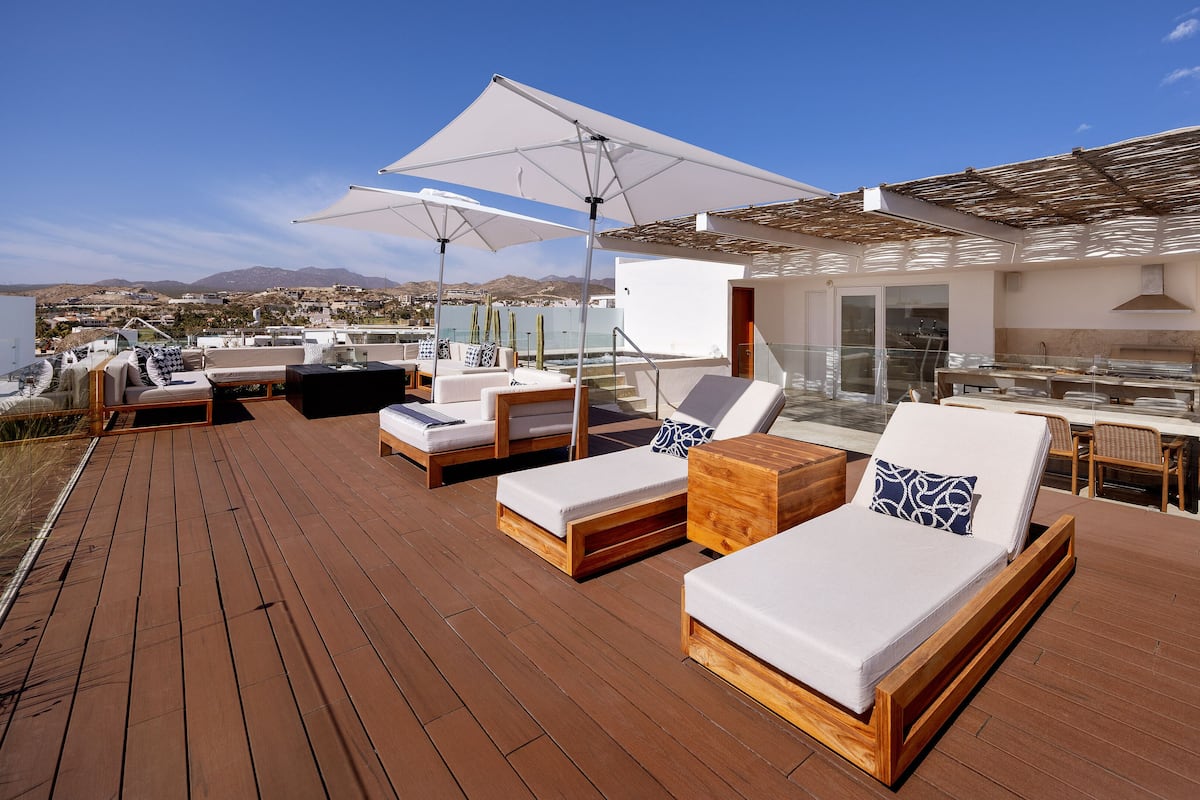 Une terrasse sur le toit avec un plancher en bois, des chaises longues et des parasols.