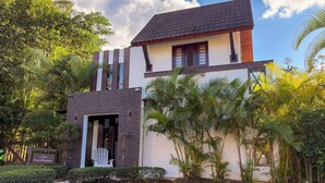 Una villa moderna con struttura su due piani, un ingresso ben visibile e rigogliosa vegetazione tropicale.