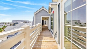 A wooden deck leading to a building with large windows and a white railing. - Lala Land TC 6302 (Port Aransas)