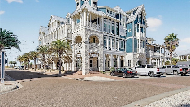 A large, multi-story building with a prominent balcony, a stone facade, and a clear blue sky. - Lala Land TC 6302 (Port Aransas)