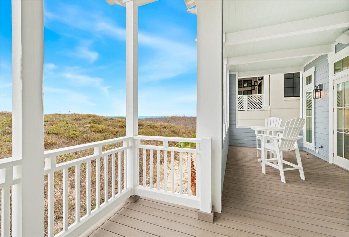 A covered outdoor area with a wooden deck, white railings, and a table with chairs.