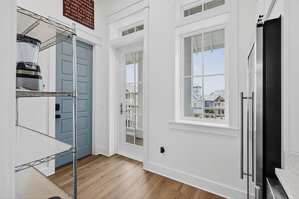 A kitchen with white walls, a blue door, and a large window.