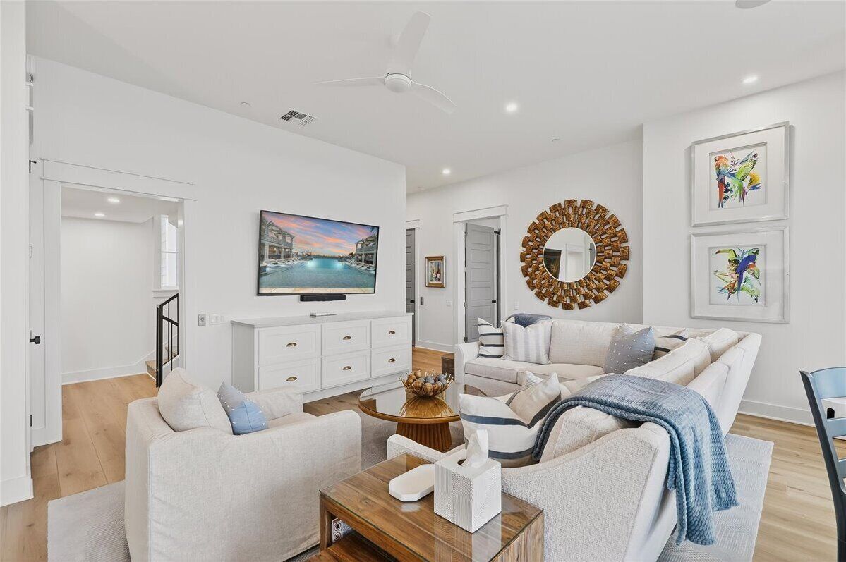 A modern living room with a flat-screen TV, a round mirror, and artwork on the walls.