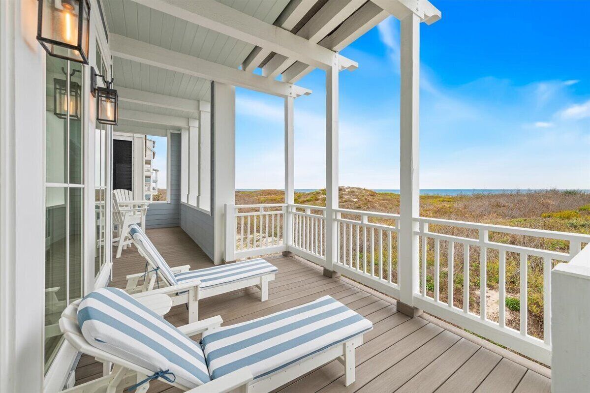 Eine überdachte Veranda mit zwei Loungestühlen und Blick auf den Strand.