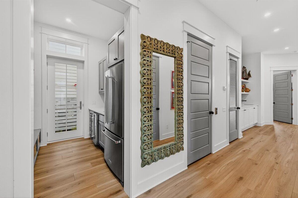 Una cocina moderna con armarios blancos, un refrigerador de acero inoxidable y un espejo decorativo con un marco ornamentado.