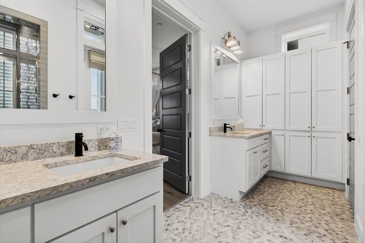 A modern bathroom with white cabinetry, a black door, and a marble countertop.