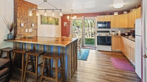 A kitchen with wooden cabinets, a central island with stools, a dining table, and a view to the outdoors. - Château Rouge 212 ~ Lazy M Lodge (Red Lodge)